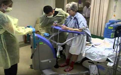 two hospital professionals assisting a patient standing with a machine in a hospital room
