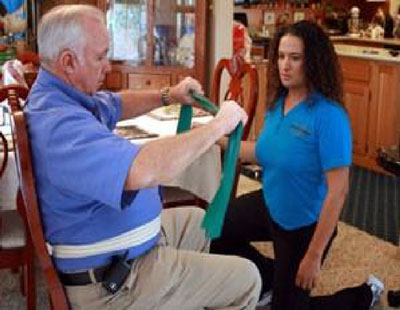 physical therapy professional assiting a seated patient with an exercise inside the home