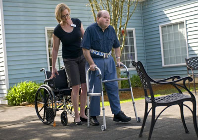 physical therapy professional assisting a patient using a walker on an outdoor patio