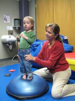 physical therapy professional supporting a child standing on a padded surface