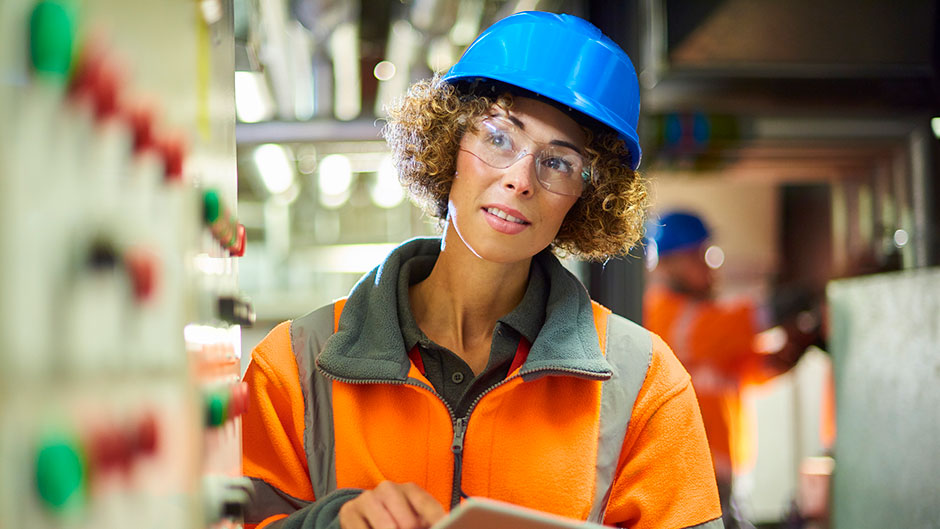 Industrial Maintenance technician looking at equipment and holding a clipboard with paper