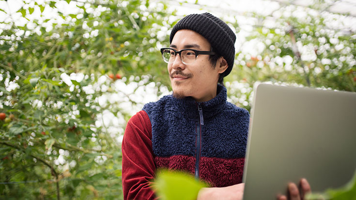 Student outdoors with a laptop, smiling and looking offscreen