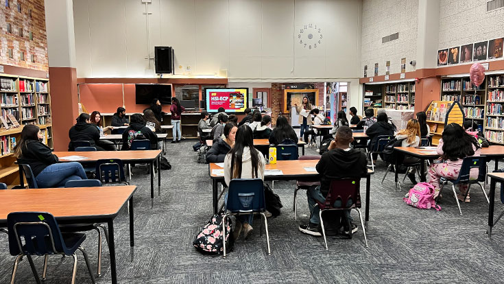 students at tables in a library or classroom