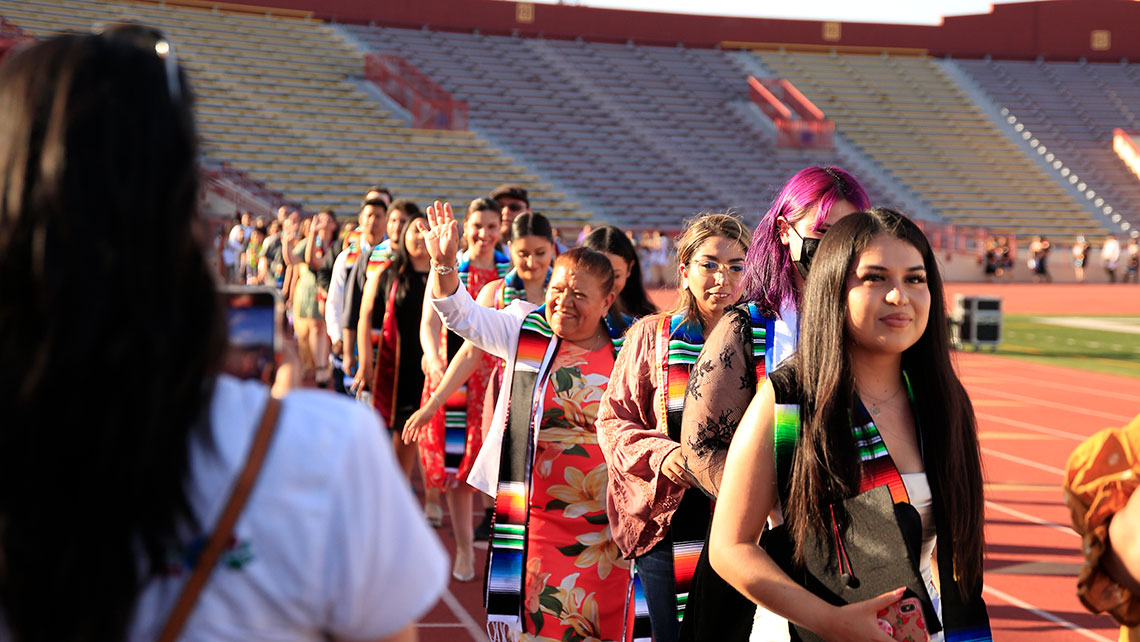 group photo of graduates walking in a row inside Hughes Stadium