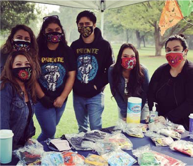 a group of Puente students posing in front of a table outdoors, and wearing masks